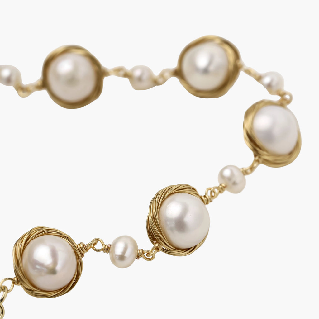 Gold wire-wrapped freshwater pearl bracelet with alternating pearl sizes on cream background, adjustable length