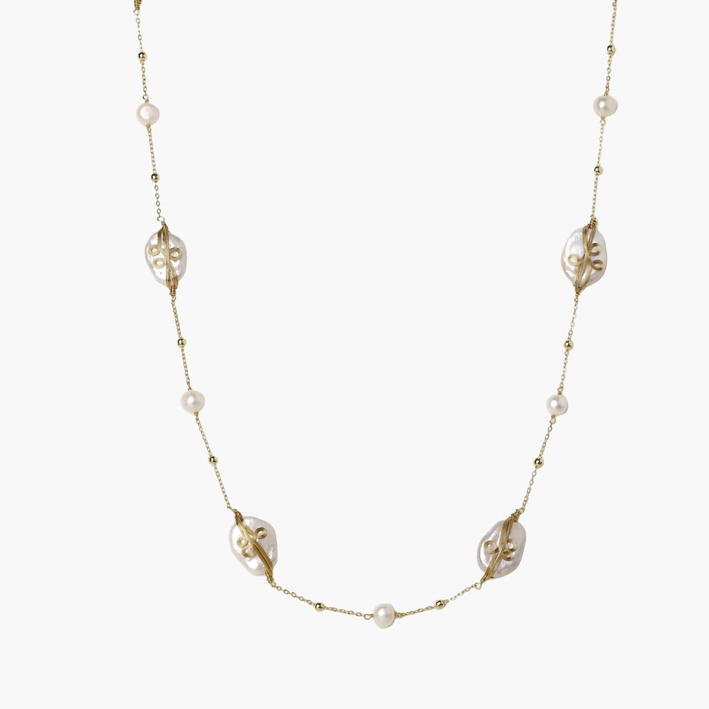 Long gold chain necklace with baroque pearls wrapped in leaf designs and small freshwater pearls spaced along the strand