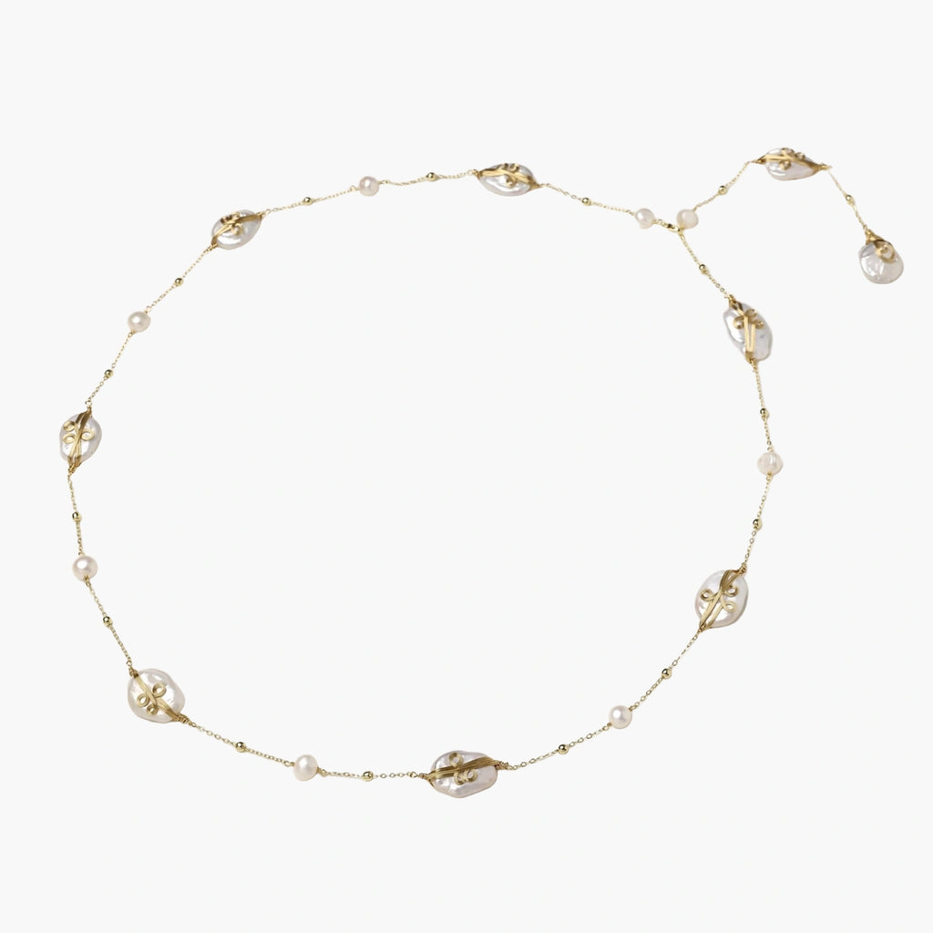 Long gold chain necklace with baroque pearls wrapped in leaf designs and small freshwater pearls spaced along the strand