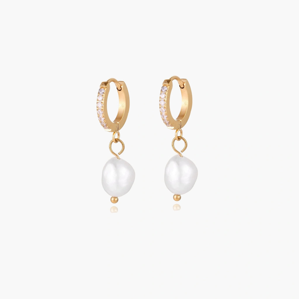 Gold huggie hoop earrings with pavé crystals and white freshwater pearl drops on cream background