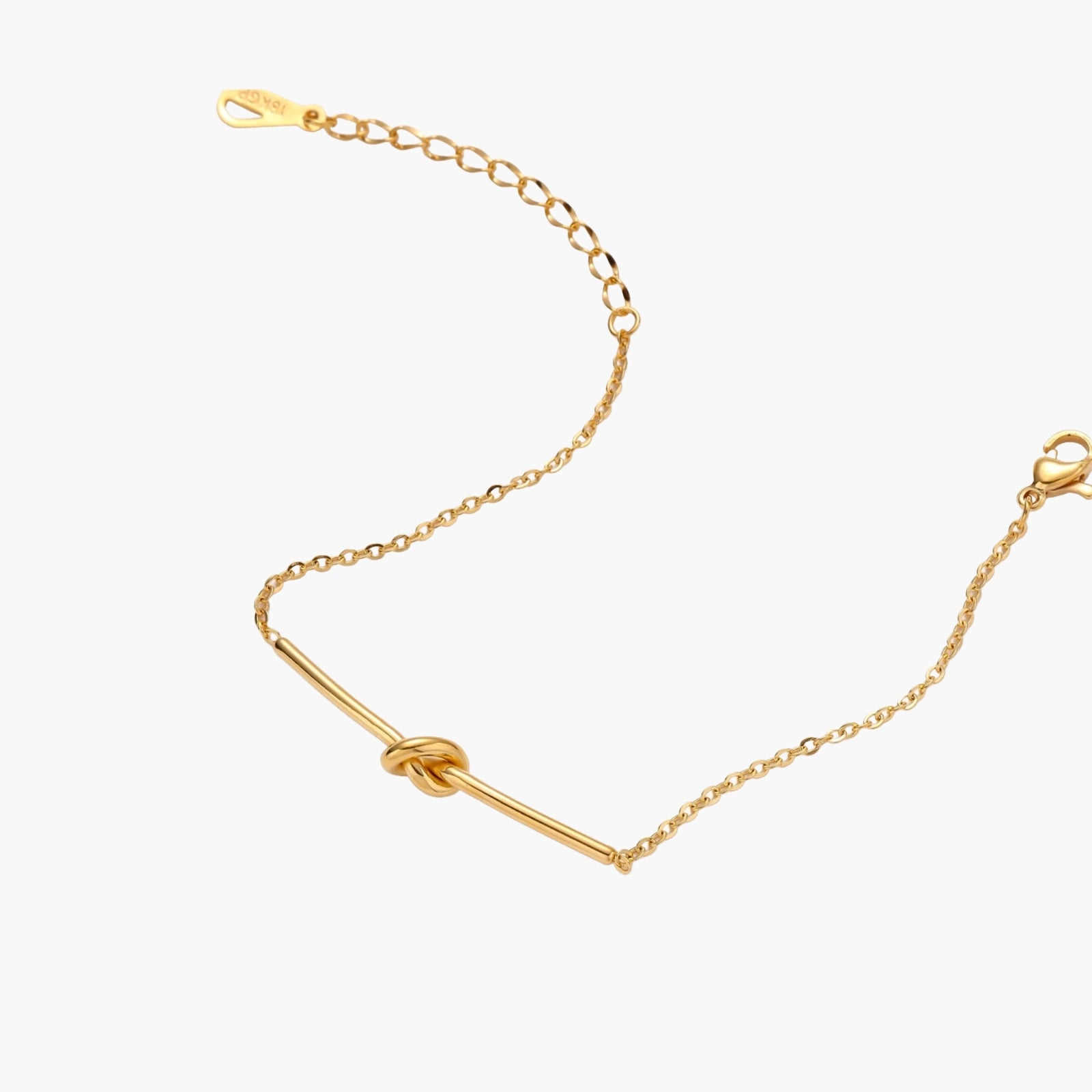 Delicate gold chain bracelet with minimalist bar and centered knot detail on cream background