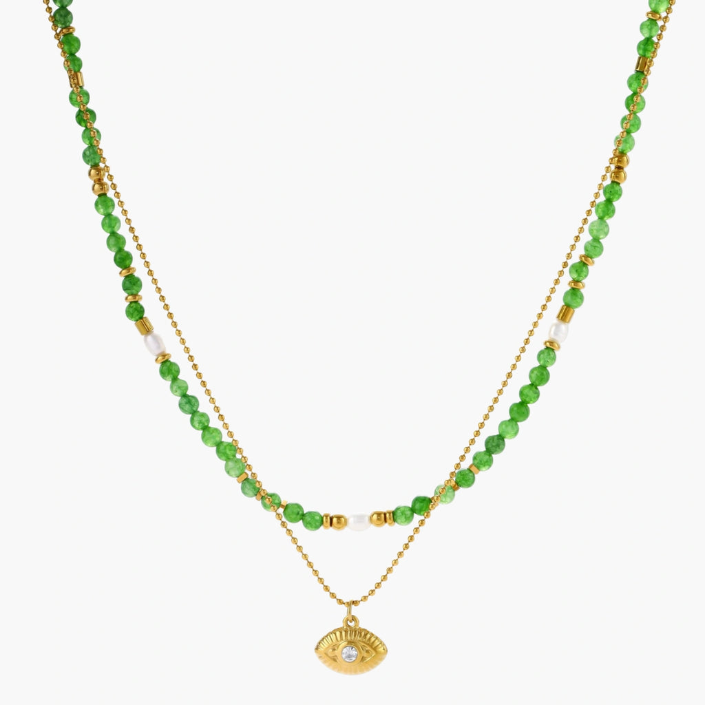 Layered necklace with green stone beads, gold spacers, white accents, and protective eye pendant on cream background.
