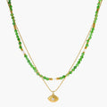Layered necklace with green stone beads, gold spacers, white accents, and protective eye pendant on cream background.