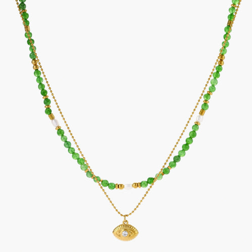 Layered necklace with green stone beads, gold spacers, white accents, and protective eye pendant on cream background.